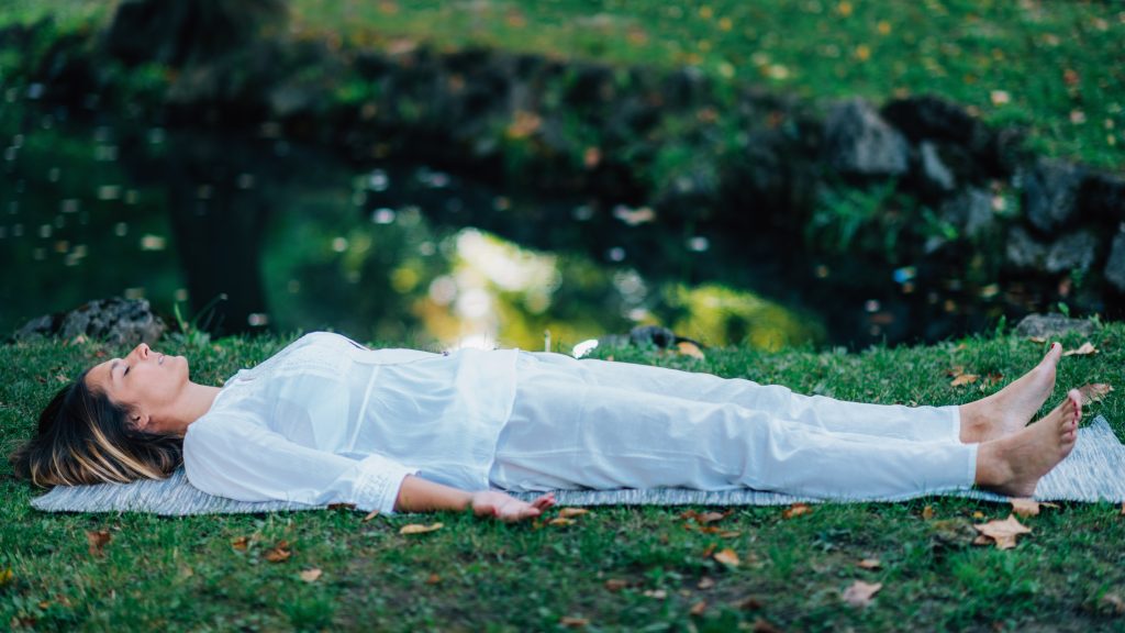 Corpse Position, Savasana, Meditation. Young woman practicing yoga and meditating by the water.