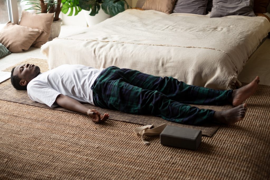 Young black man lying in Dead Body exercise or Corpse pose with his eyes closed, Savasana pose, working out, resting after practice